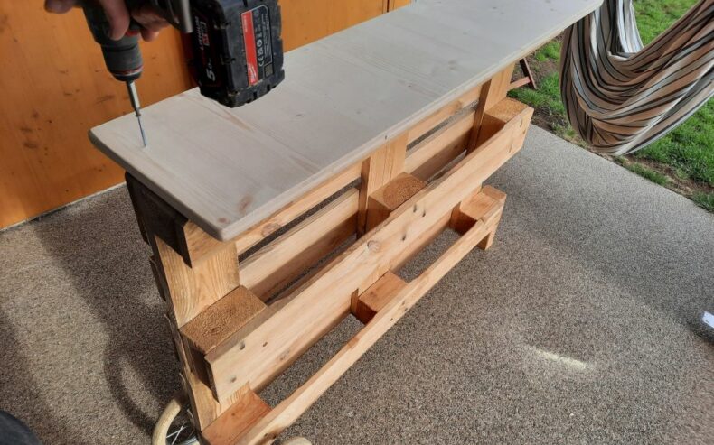 Holzplatte auf der Oberseite der Palette mittig mit 4 Schrauben befestigen.
