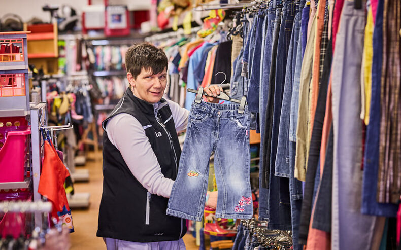 Caritas Mitarbeiterin zeigt eine Kinderjeans im Second Hand Laden her.