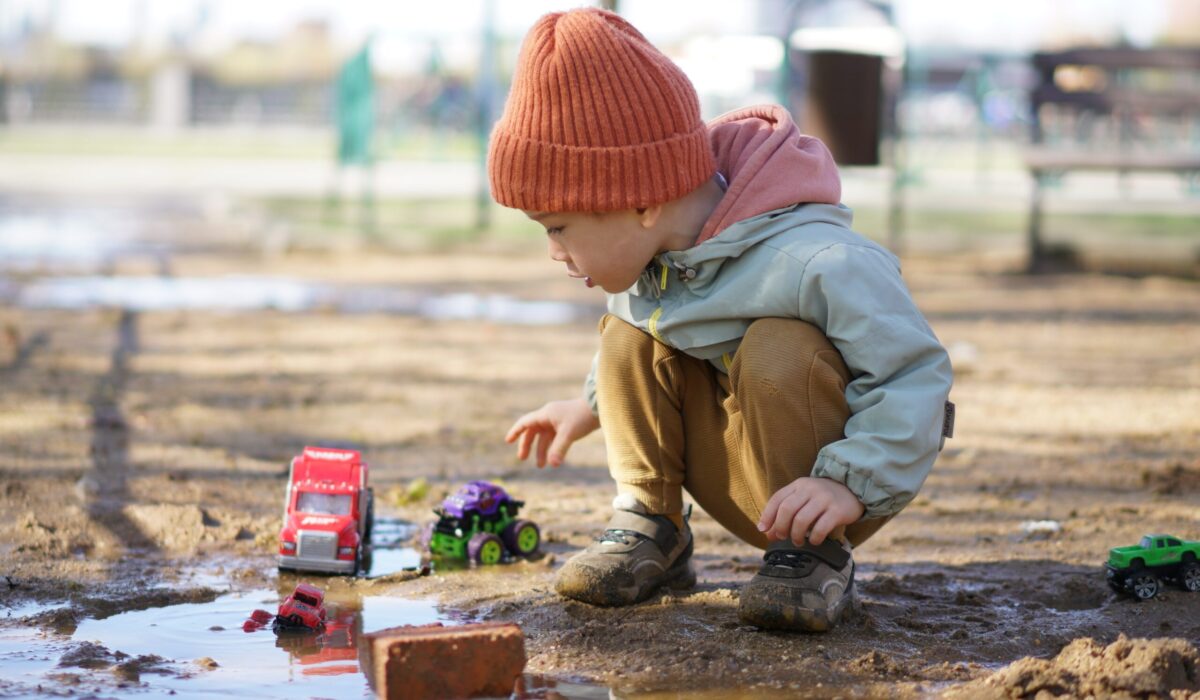 Kleiner Junge hockt in einer Schlammpfütze und spielt mit seinen Plastikspielzeugautos.