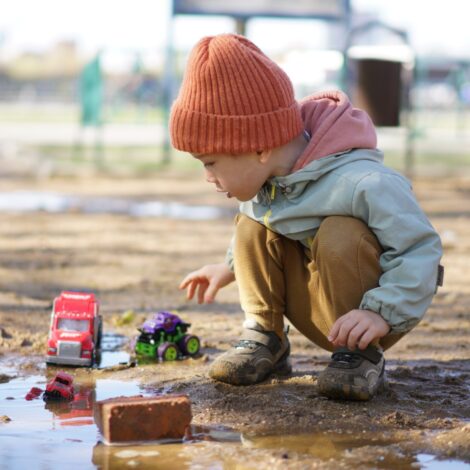 Kleiner Junge hockt in einer Schlammpfütze und spielt mit seinen Plastikspielzeugautos.