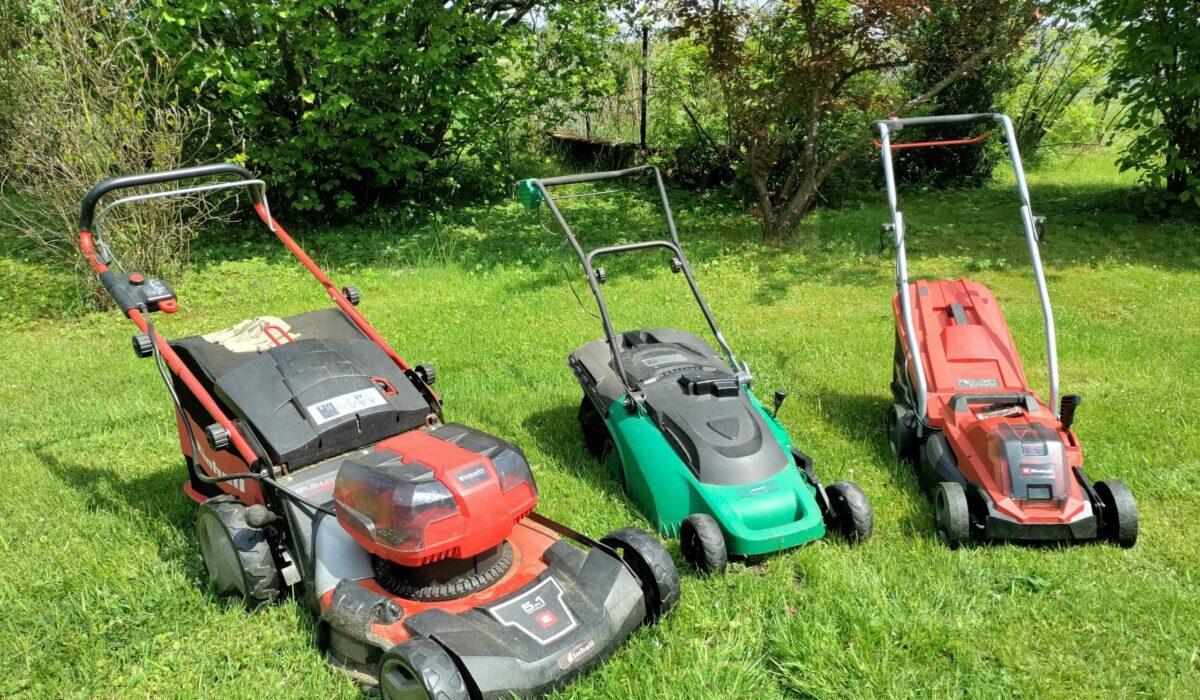 Drei verschiedene Rasenmäher nebeneinander auf der Wiese