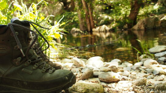 Wanderschuhe stehen am Ufer eines Baches.