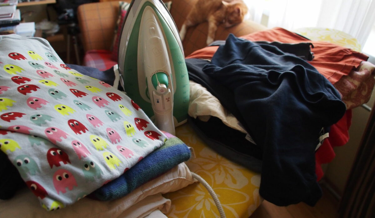 Wäschestapel und Bügeleisen, im Hintergrund eine schlafende Katze.