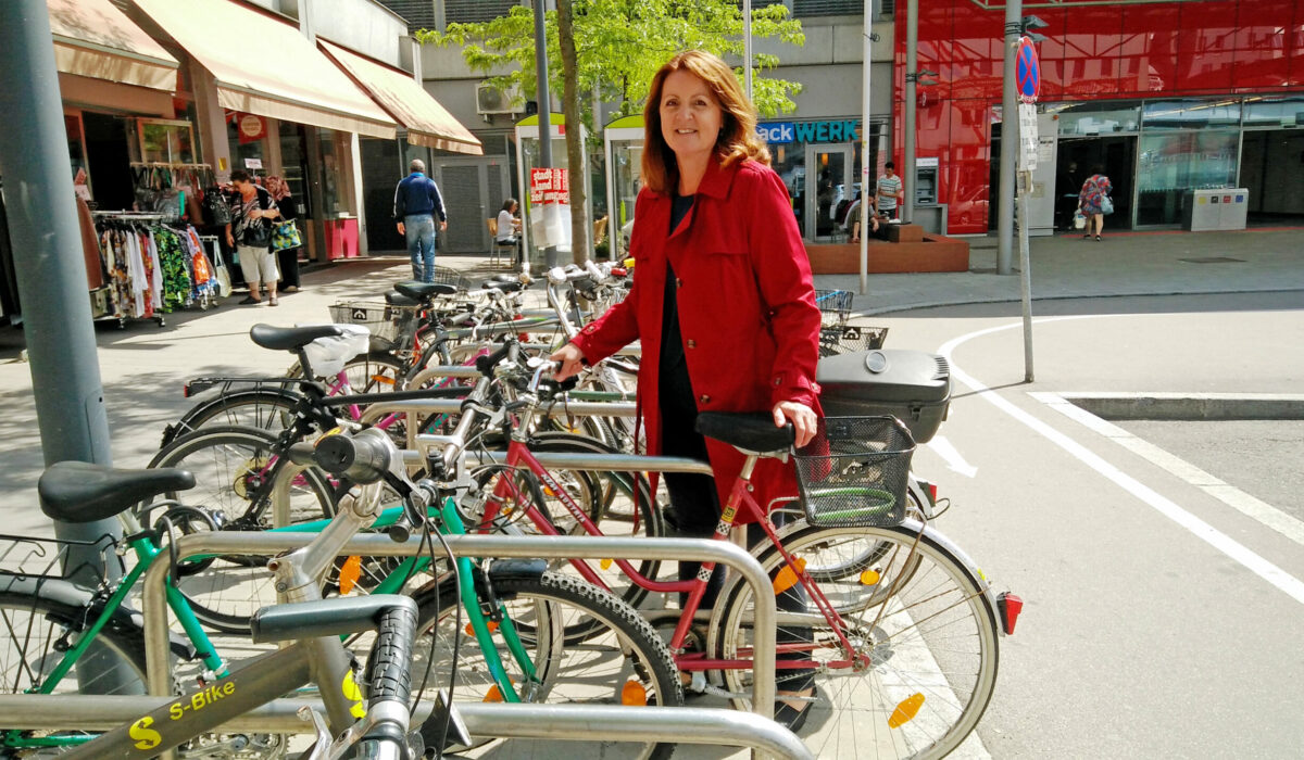 Christa stellt ihr Fahrrad am Bahnhof am Radständer ab.