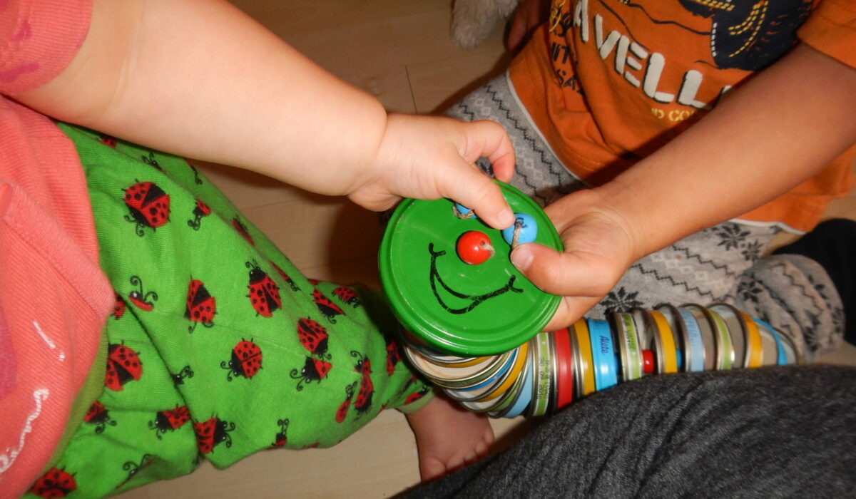 Kinder spielen mit einer selbstgebastelten Raute aus Metalldeckeln.