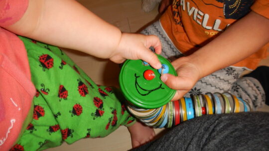 Kinder spielen mit einer selbstgebastelten Raute aus Metalldeckeln.