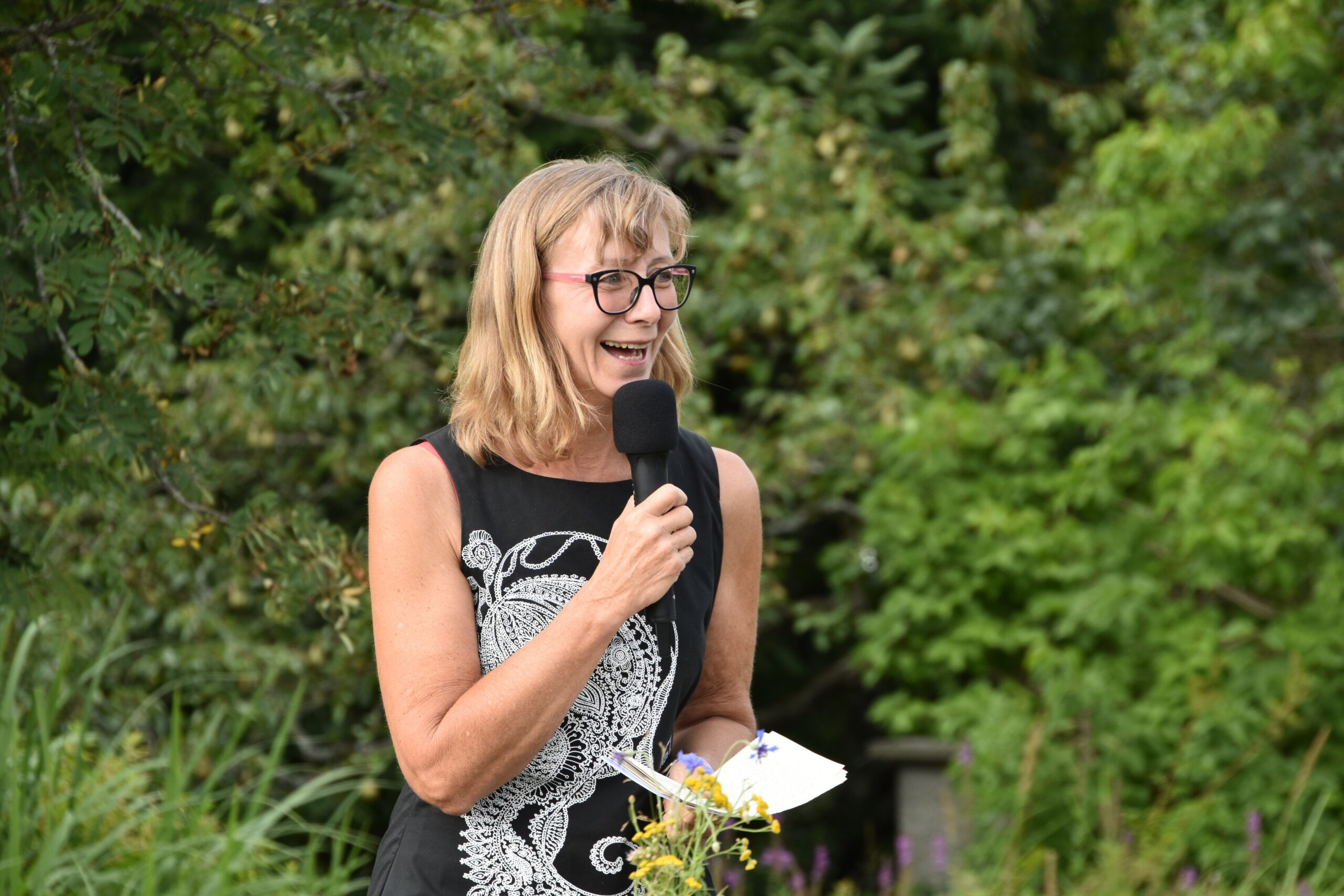 Elisabeth Koppensteiner mit Mikrofon vor grünen Bäumen