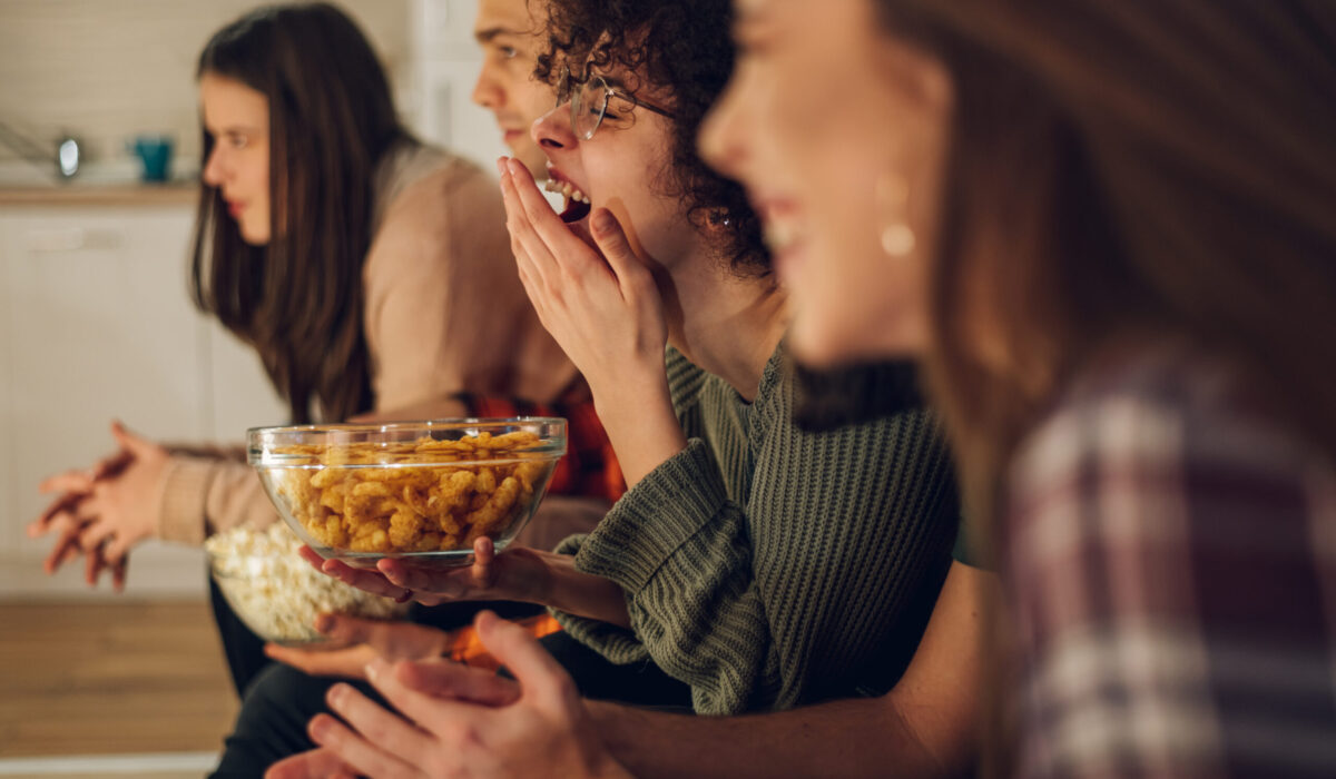 Freunde entspannen sich gemeinsam zu Hause, schauen fern und essen Snacks. Sie sehen sich den Eurovision Song Contest an.