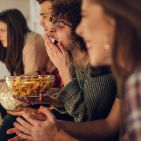 Freunde entspannen sich gemeinsam zu Hause, schauen fern und essen Snacks. Sie sehen sich den Eurovision Song Contest an.