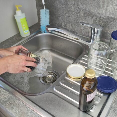 Hände entfernen Etiketten mit Hausmitteln von Gläsern im Waschbecken