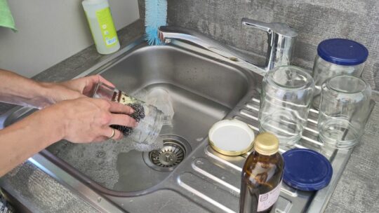 Hände entfernen Etiketten mit Hausmitteln von Gläsern im Waschbecken