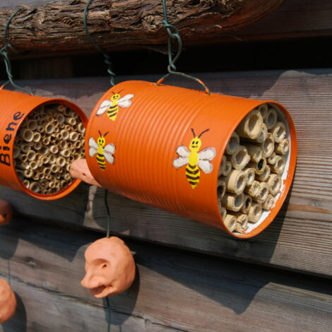 Zwei orange bemalte Dosen mit aufgemalten Bienen und mit Bambus und Schilf gefüllt