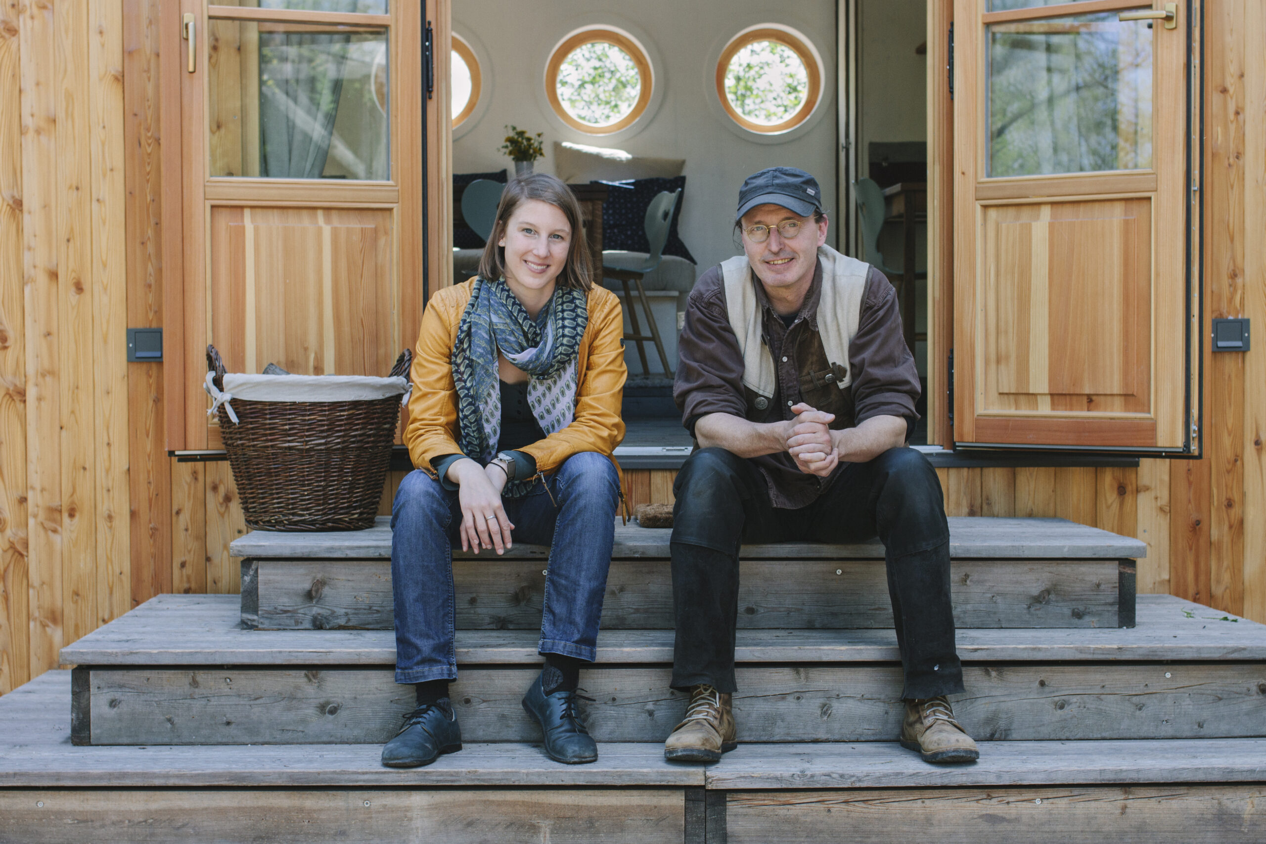 Theresa Mai und Christian Frantal sind die Gründer von Wohnwagon und sitzen gemeinsam auf Stufen eines Tiny Houses