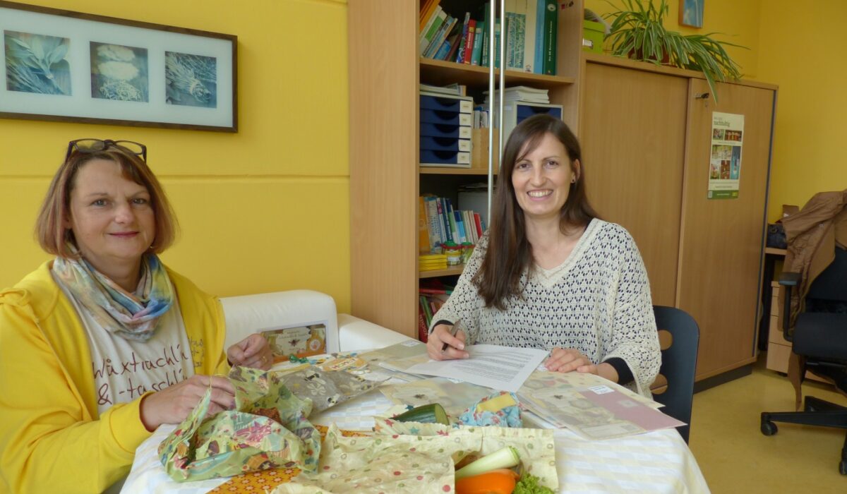 Barbara Apfelthaler und Petra Nemec sitzen an einem Tisch auf dem Wachstücher liegen.
