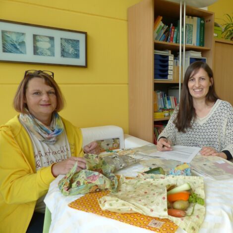 Barbara Apfelthaler und Petra Nemec sitzen an einem Tisch auf dem Wachstücher liegen.