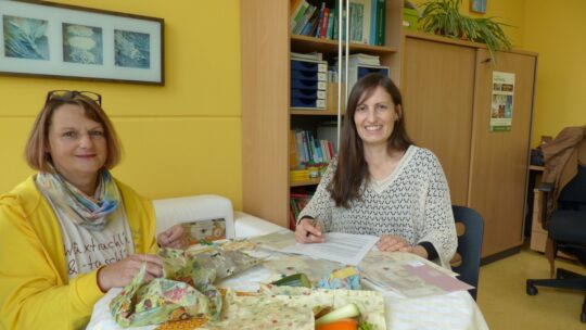 Barbara Apfelthaler und Petra Nemec sitzen an einem Tisch auf dem Wachstücher liegen.