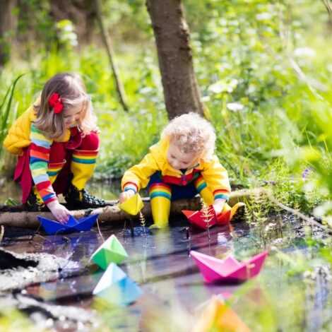 Zwei Kinder spielen mit Papierbooten am Bach.
