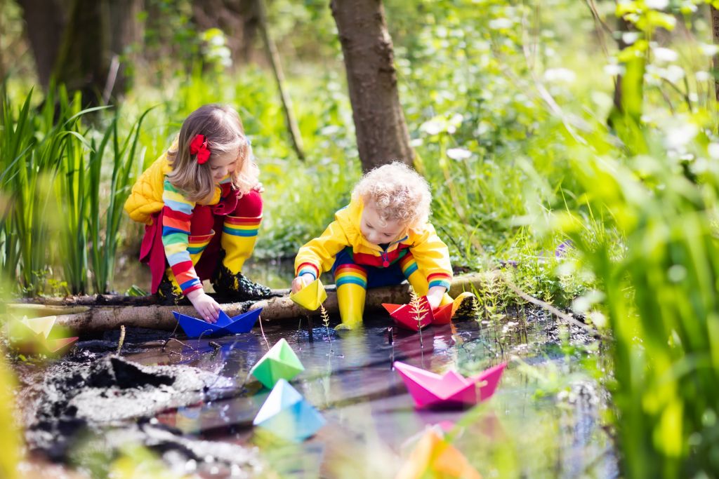 Zwei Kinder spielen mit Papierbooten am Bach.