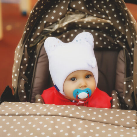 Baby mit Mütze schaut aus dem Kinderwagen.