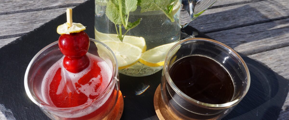 Cold Brew Kaffee, Leitungswasser und ein alkoholfreier Drink in schönen Gläsern stehen auf einem Gartentisch