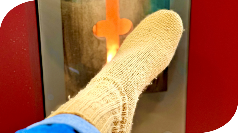 Mann wärmt seinen Fuß mit gelben Wollsocken vor dem Ofenfenster