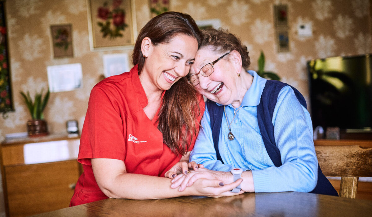 Mitarbeiterin der Caritas umarmt ältere Dame.