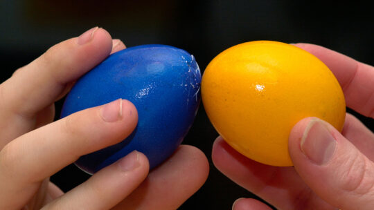 zwei Kinder mit einem blauen und einem gelben Ei beim Eierpecken