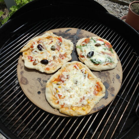 Drei kleine Pizzen auf einem Pizzastein auf einem Griller.
