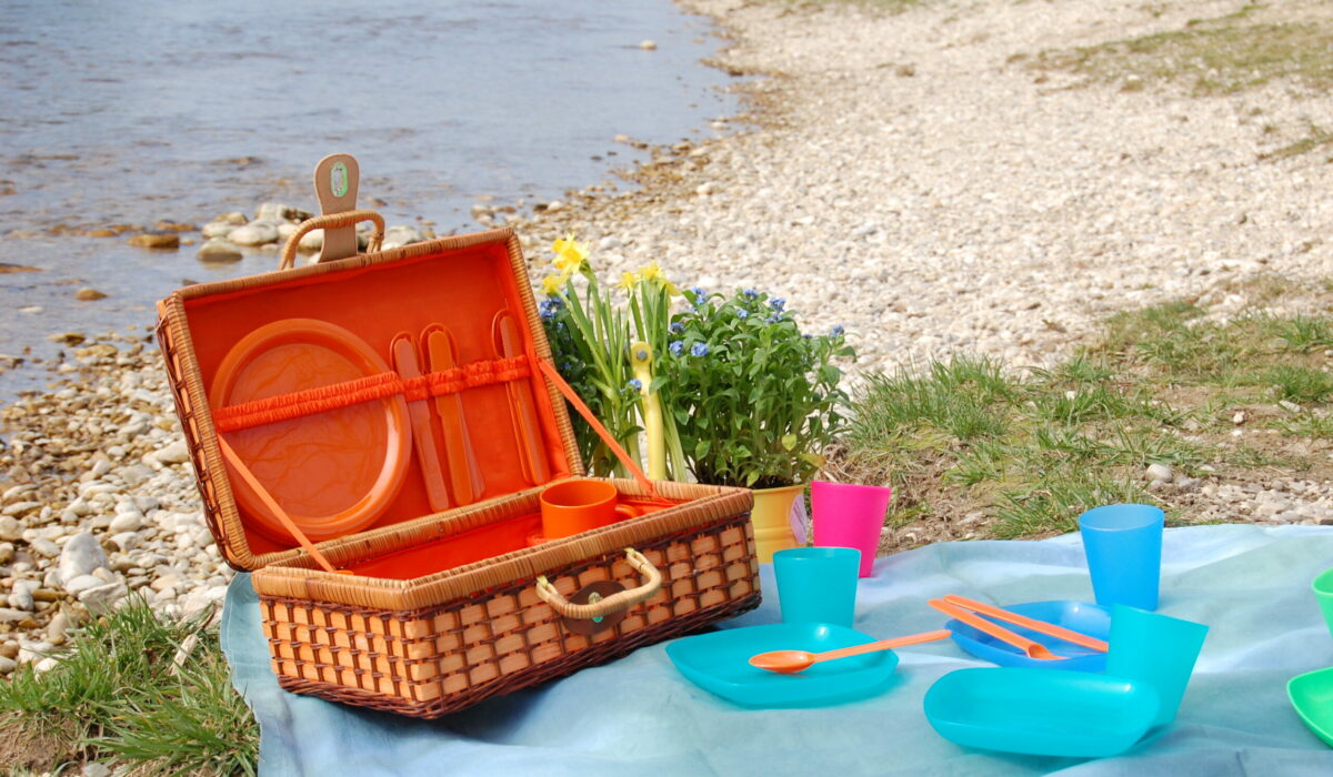 Picknick-Korb in der Natur mit bunten Plastiktellern, Bechern und Plastikbesteck.