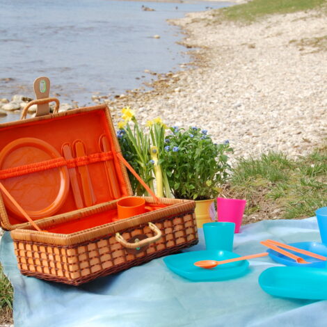 Picknick-Korb in der Natur mit bunten Plastiktellern, Bechern und Plastikbesteck.