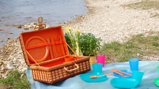 Picknick-Korb in der Natur mit bunten Plastiktellern, Bechern und Plastikbesteck.