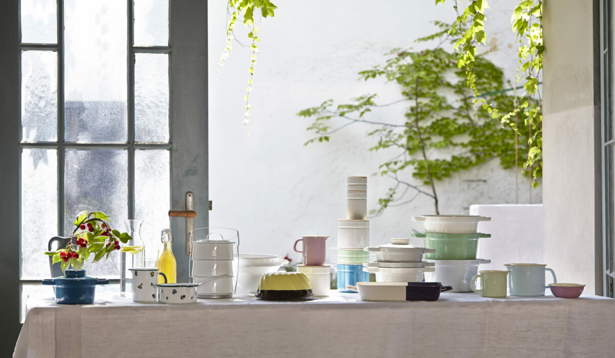 Geschirrwaren von Riess stehen auf einen Tisch mit weißem Tischtuch im Hintergrund eine Holz-Glastür und eine grüne Zimmerpflanze