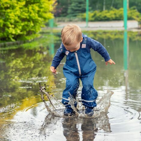 Kind mit Regenhose springt in eine Pfütze.