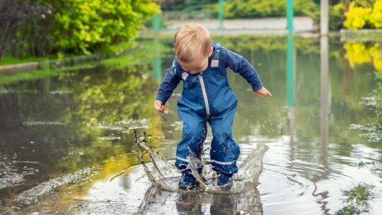 Kind mit Regenhose springt in eine Pfütze.