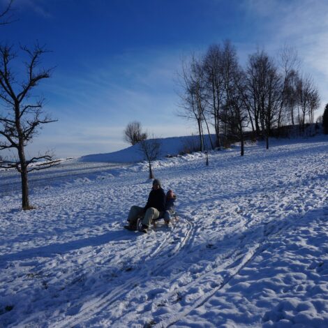 Mutter und Tochter beim Rodeln auf einer verschneiten Wiese.