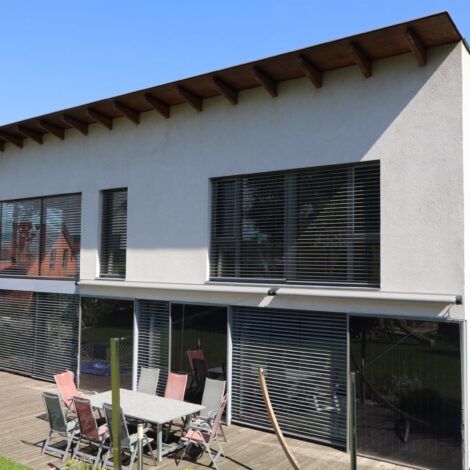 Passivhaus mit Raffstores und Gartenmöbeln auf der Terrasse.
