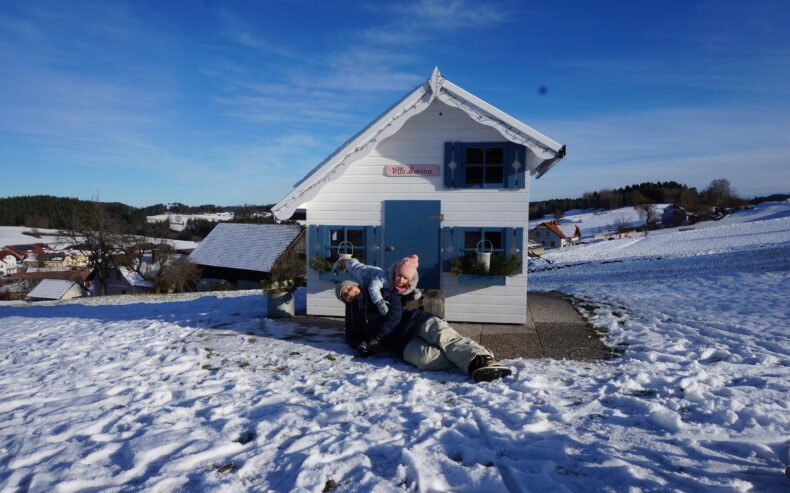 Mutter und Tochter tollen im Schnee vor Spielhaus