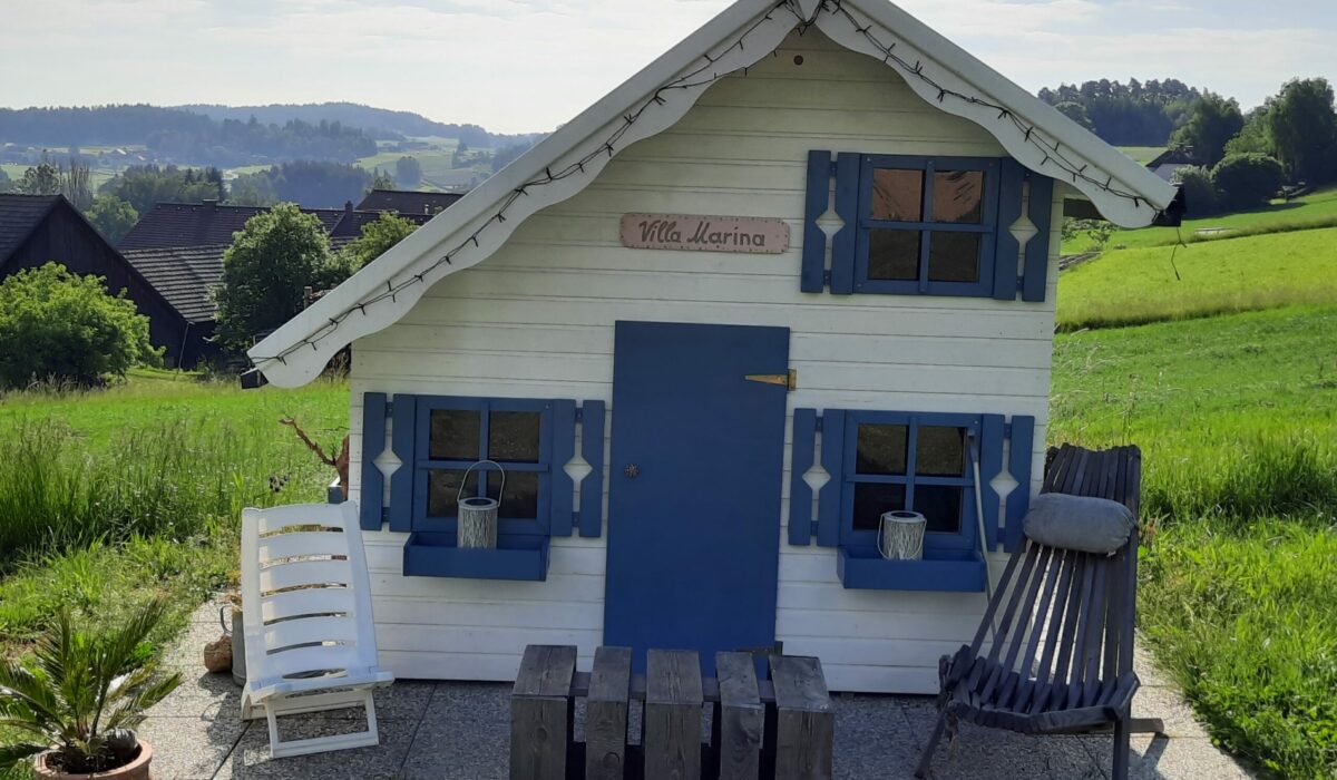Wweiß-blaues Holzspielhaus auf grüner Wiese