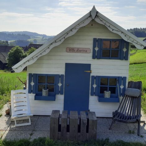 Wweiß-blaues Holzspielhaus auf grüner Wiese