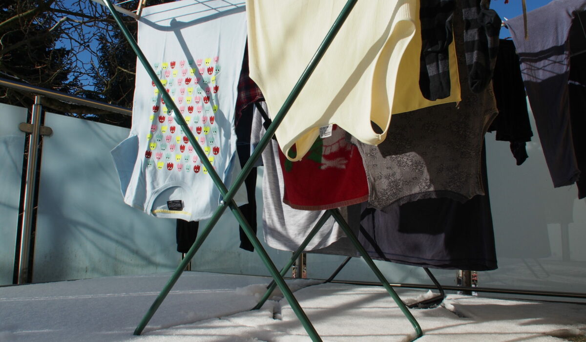 Bunte Wäsche hängt auf Wäschetrockner auf verschneiten und sonnigen Balkon