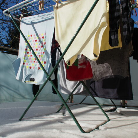 Bunte Wäsche hängt auf Wäschetrockner auf verschneiten und sonnigen Balkon