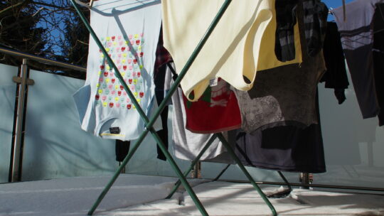 Bunte Wäsche hängt auf Wäschetrockner auf verschneiten und sonnigen Balkon