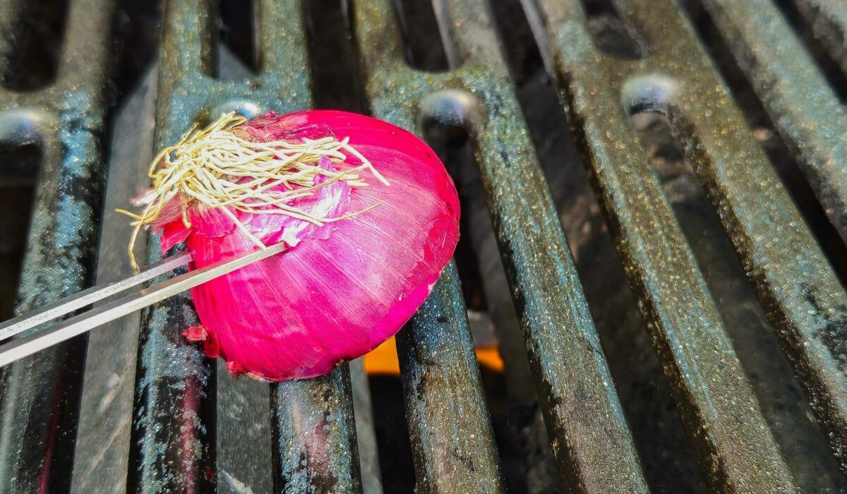 Mit einer halbierten Zwiebel wird ein Grillrost gereinigt