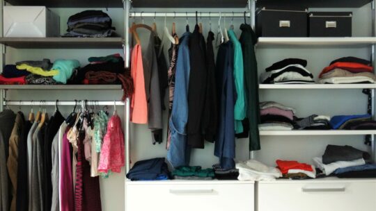 Ankleidezimmer mit vielen Kleidern und Pullis auf Regalen und Stangen