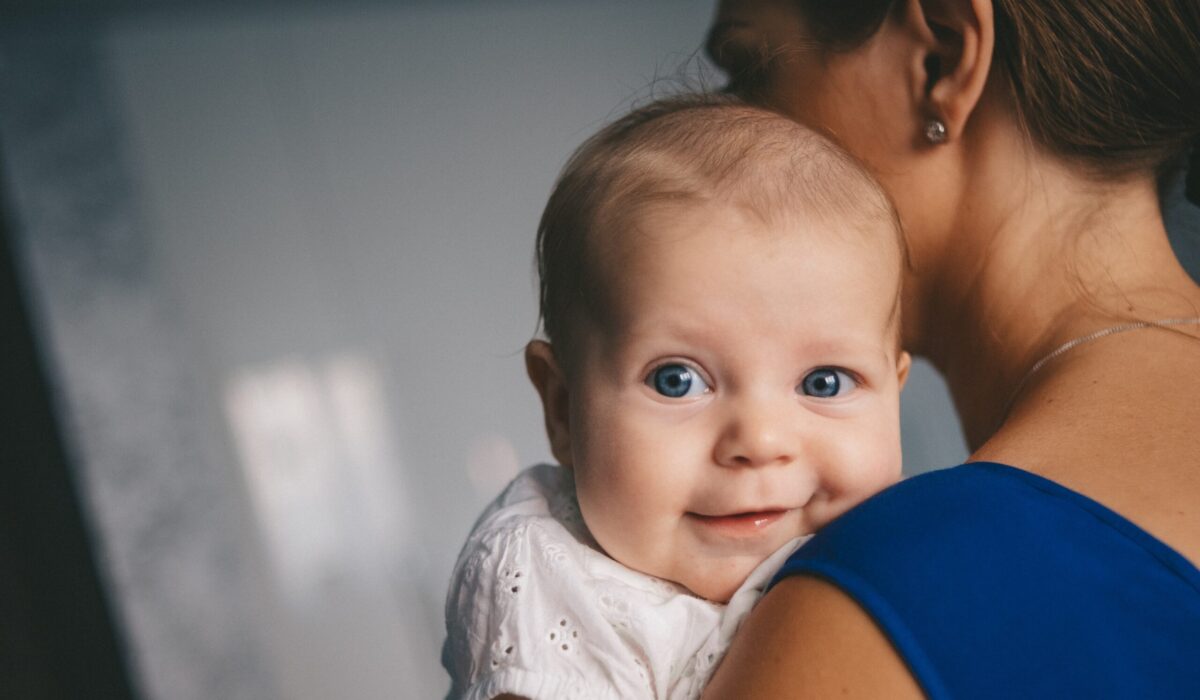 Baby lächelt über die Schulter der Mutter