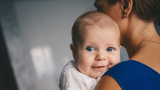Baby lächelt über die Schulter der Mutter