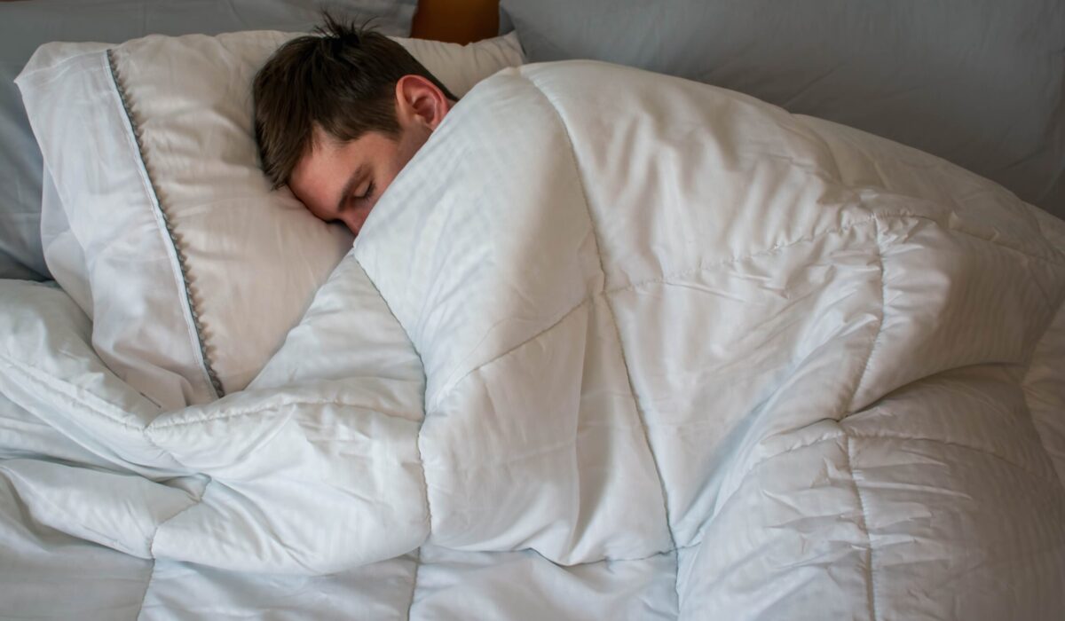 Junger Mann schläft im Bett unter einer kuscheligen Bettdecke.