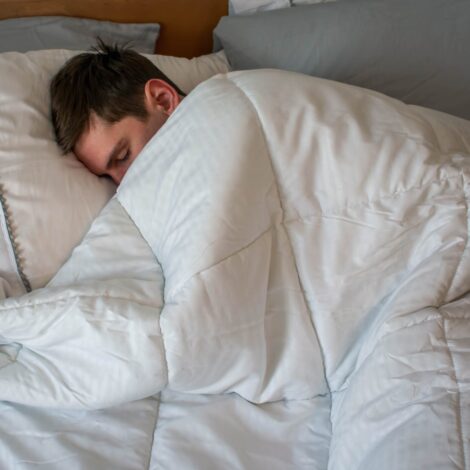 Junger Mann schläft im Bett unter einer kuscheligen Bettdecke.