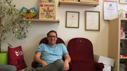 Mag. Stefan Friedrich sitzt auf alten roten Kinosessel in seinem Büro