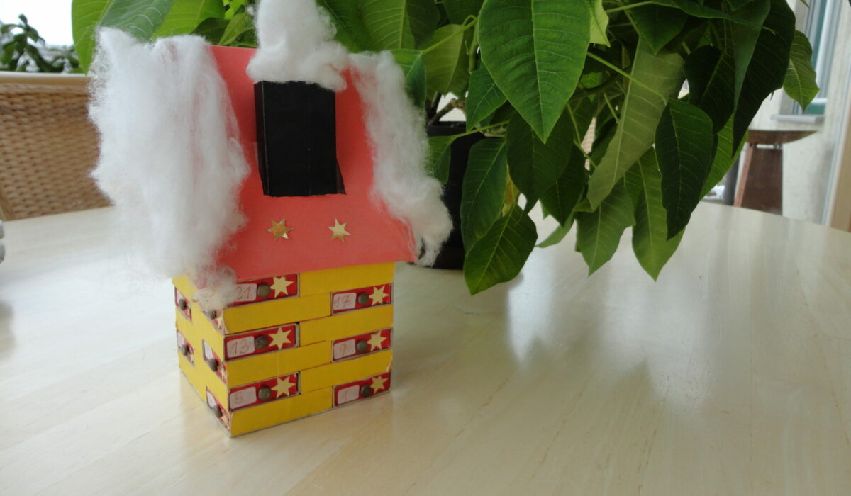 Adventkalender in Form eines Hauses mit Watte als Schnee am Dach
